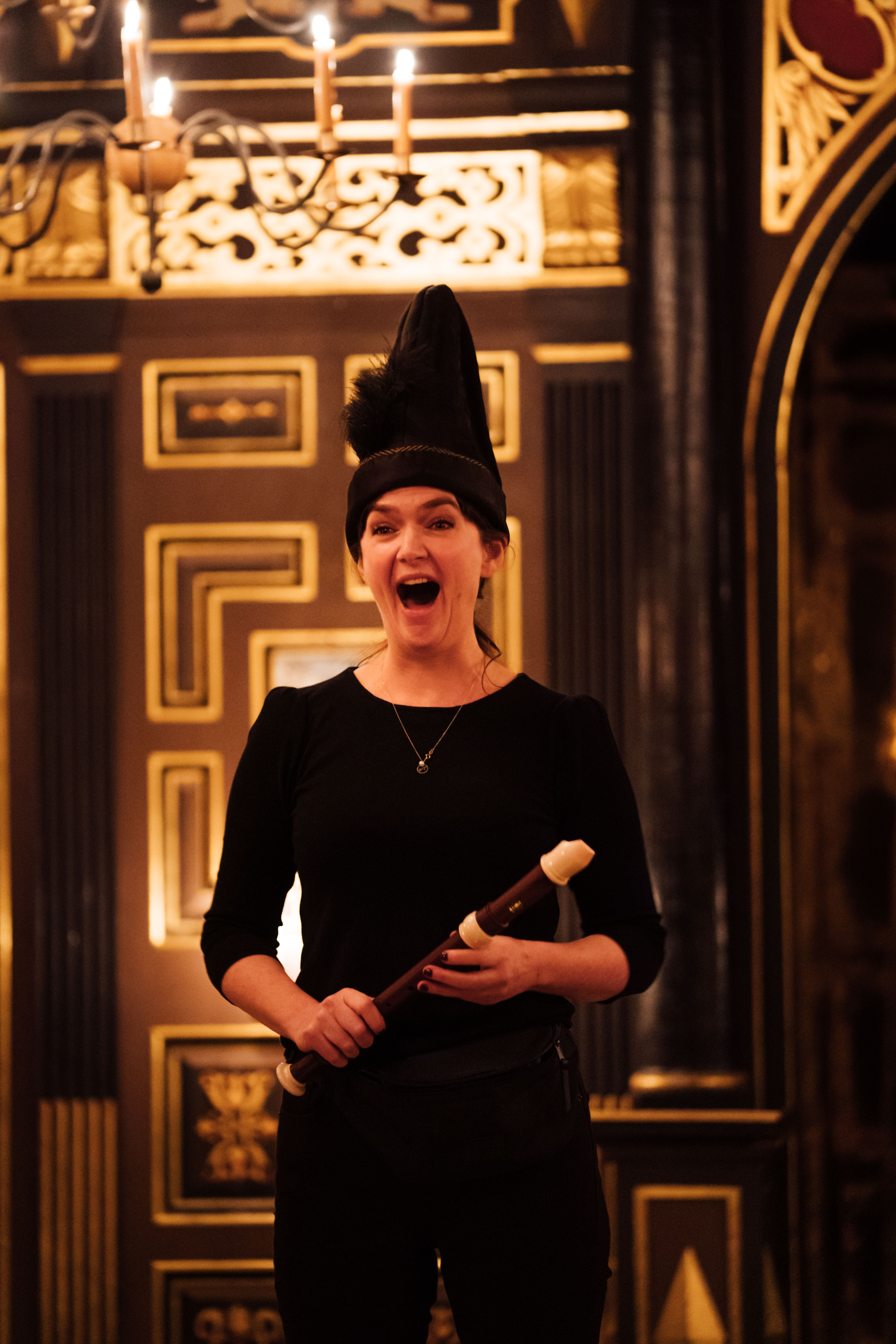 Rachael in black pointy hat, black top and trousers holding a recorder and looking excited